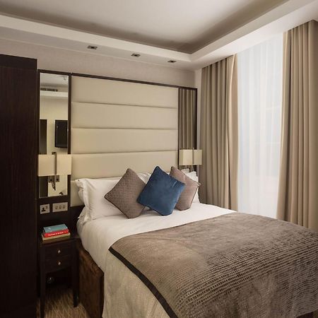 Hotel Montcalm Brewery Townhouse Londyn Zewnętrze zdjęcie The image shows a cozy bedroom. It features a comfortable double bed with a light-colored duvet and decorative pillows in shades of blue and gray. The headboard is upholstered in a soft material, and there are bedside lamps on either side of the bed.