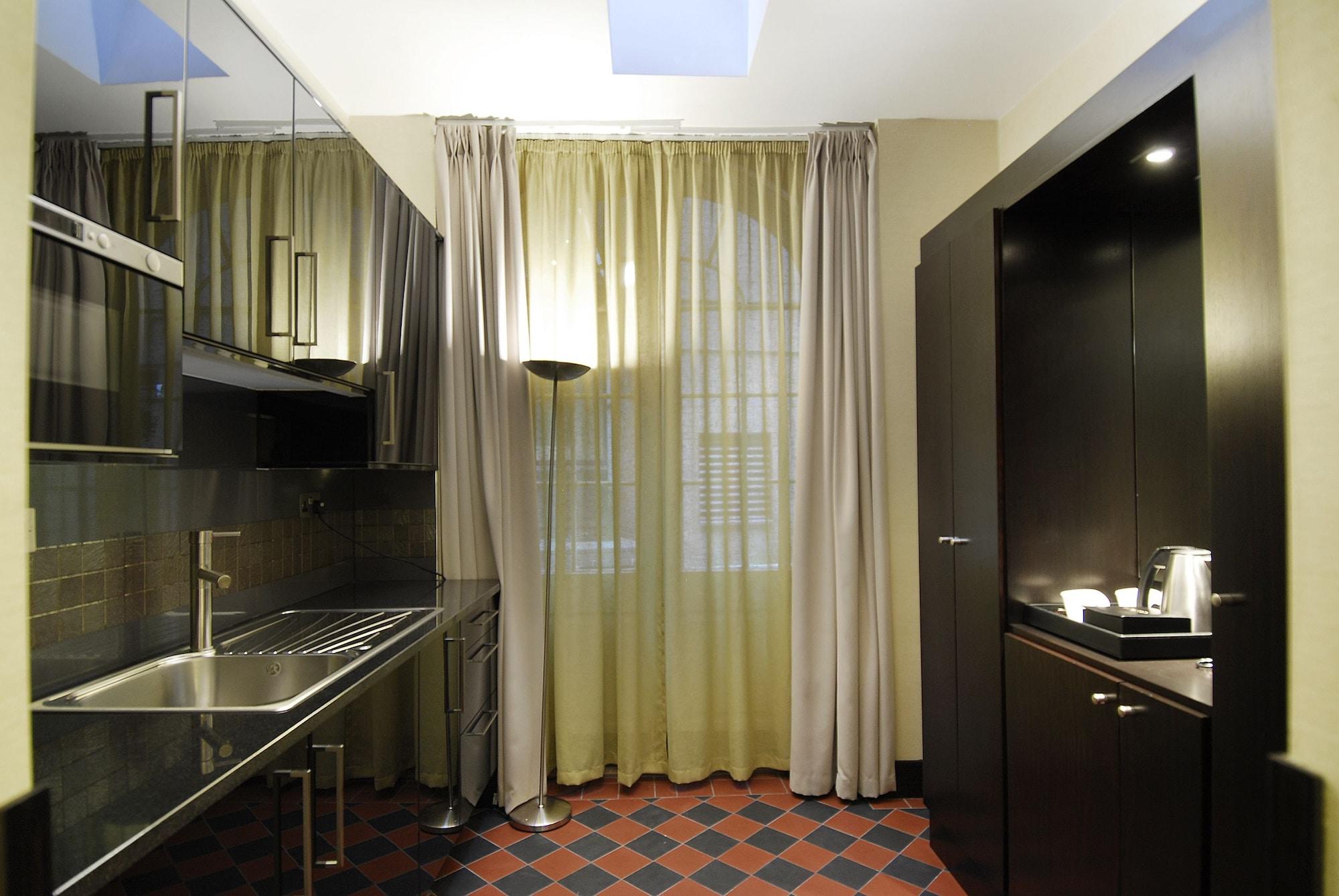Hotel Montcalm Brewery Townhouse Londyn Zewnętrze zdjęcie The photo shows a modern kitchen space. On the left side, there is a sleek countertop and kitchen cabinets in a dark finish. The backsplash appears shiny, reflecting the surroundings. To the right, there is a tall black cabinet. A window is covered w