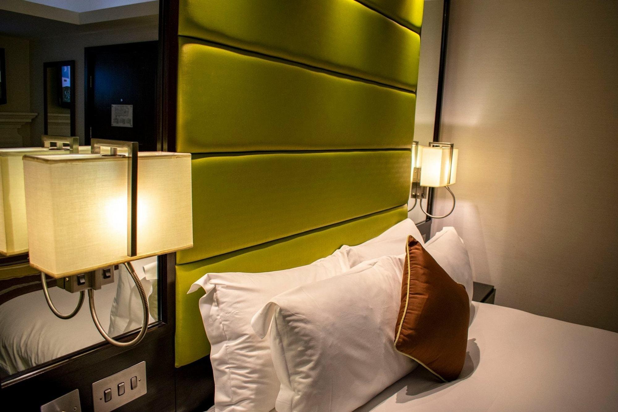 Hotel Montcalm Brewery Townhouse Londyn Zewnętrze zdjęcie The photo shows a modern hotel room with a stylish design. The focal point is a large bed with white pillows and a decorative brown pillow. The headboard is bright green and has a textured appearance. On either side of the bed, there are wall lamps t