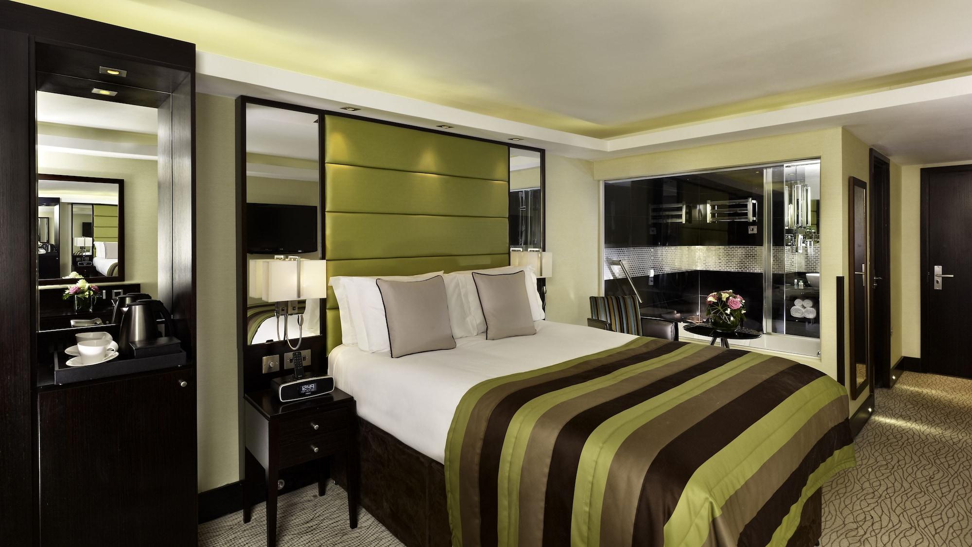Hotel Montcalm Brewery Townhouse Londyn Zewnętrze zdjęcie The photo shows a modern hotel room designed with a sophisticated aesthetic. It features a comfortable double bed with a striped brown and green bedspread, complemented by two light gray decorative pillows. Behind the bed is an elegant headboard sect