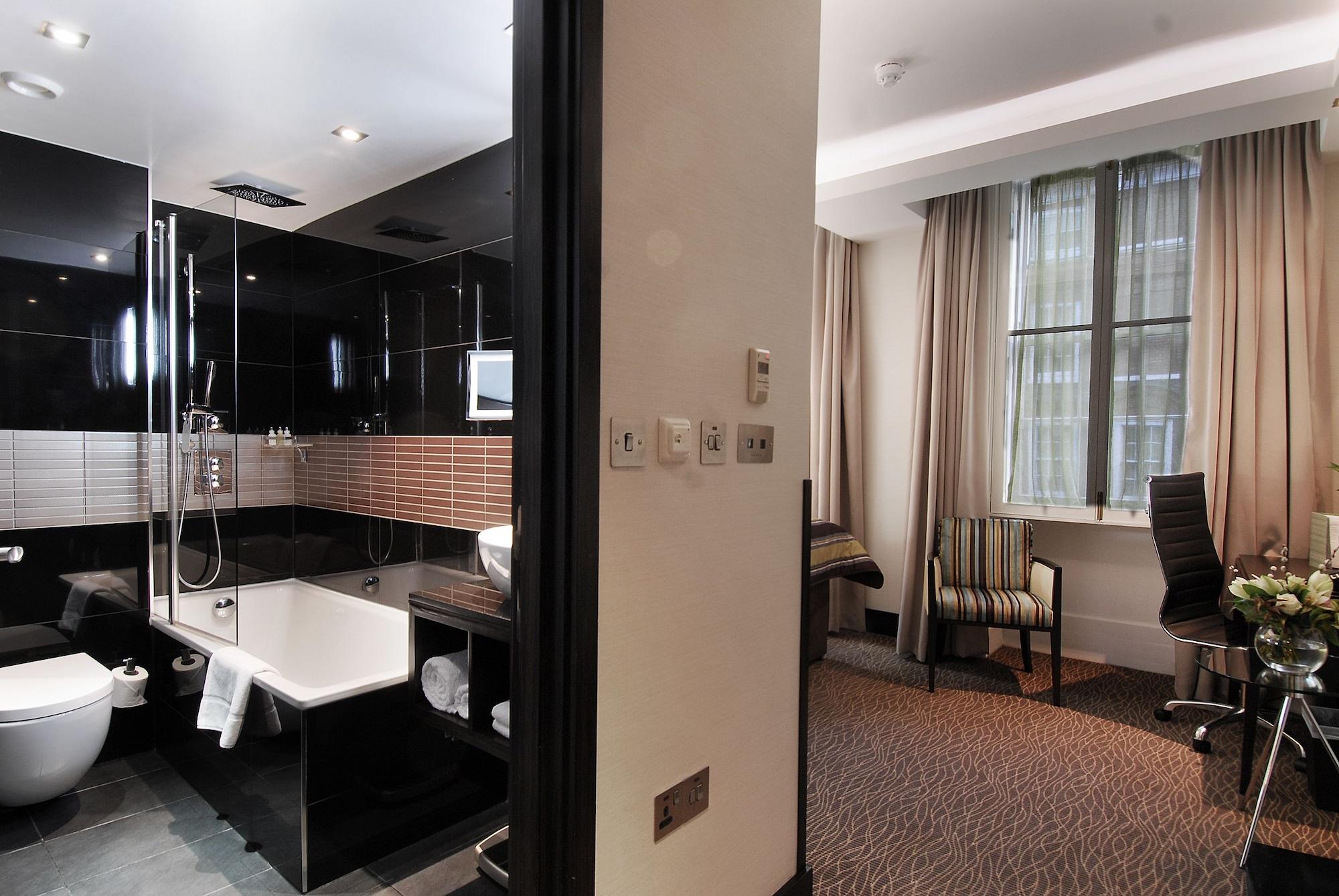 Hotel Montcalm Brewery Townhouse Londyn Zewnętrze zdjęcie The photo shows a modern hotel room that features an elegant bathroom on one side and a living area on the other. 

1. **Bathroom**: The bathroom is stylishly designed with a combination of black and white tiles. It includes a bathtub, a shower area 