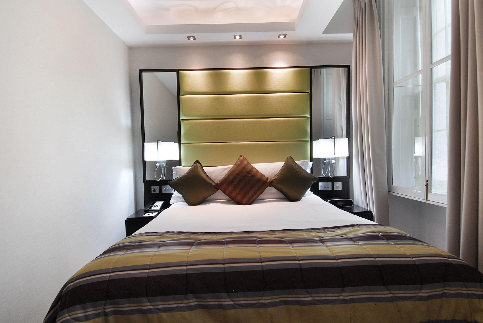 Hotel Montcalm Brewery Townhouse Londyn Zewnętrze zdjęcie The photo shows a stylishly decorated bedroom. The bed is centered in the room, featuring a white comforter with a plaid pattern in shades of brown and green. There are three decorative pillows on the bed, two in shades of brown and one in dark green