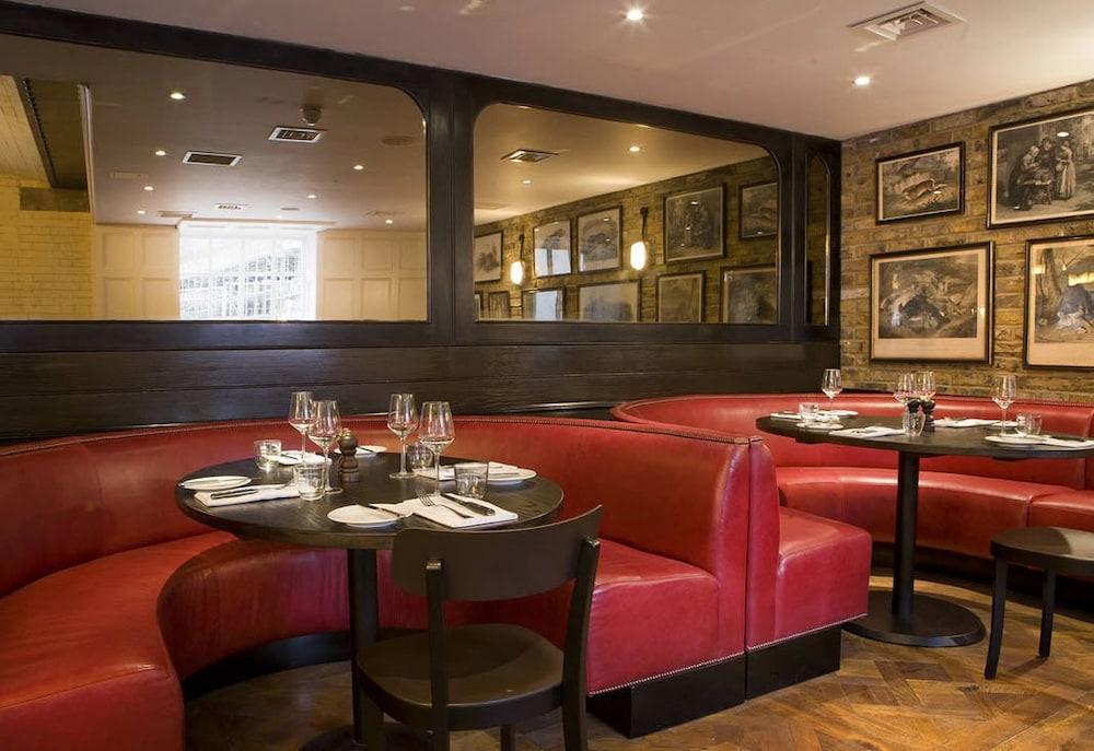 Hotel Montcalm Brewery Townhouse Londyn Zewnętrze zdjęcie The image shows the interior of a restaurant featuring a warm and inviting atmosphere. There are several round tables surrounded by black chairs, with red, upholstered booths lining the walls. The decor includes framed artwork hanging on the walls, a