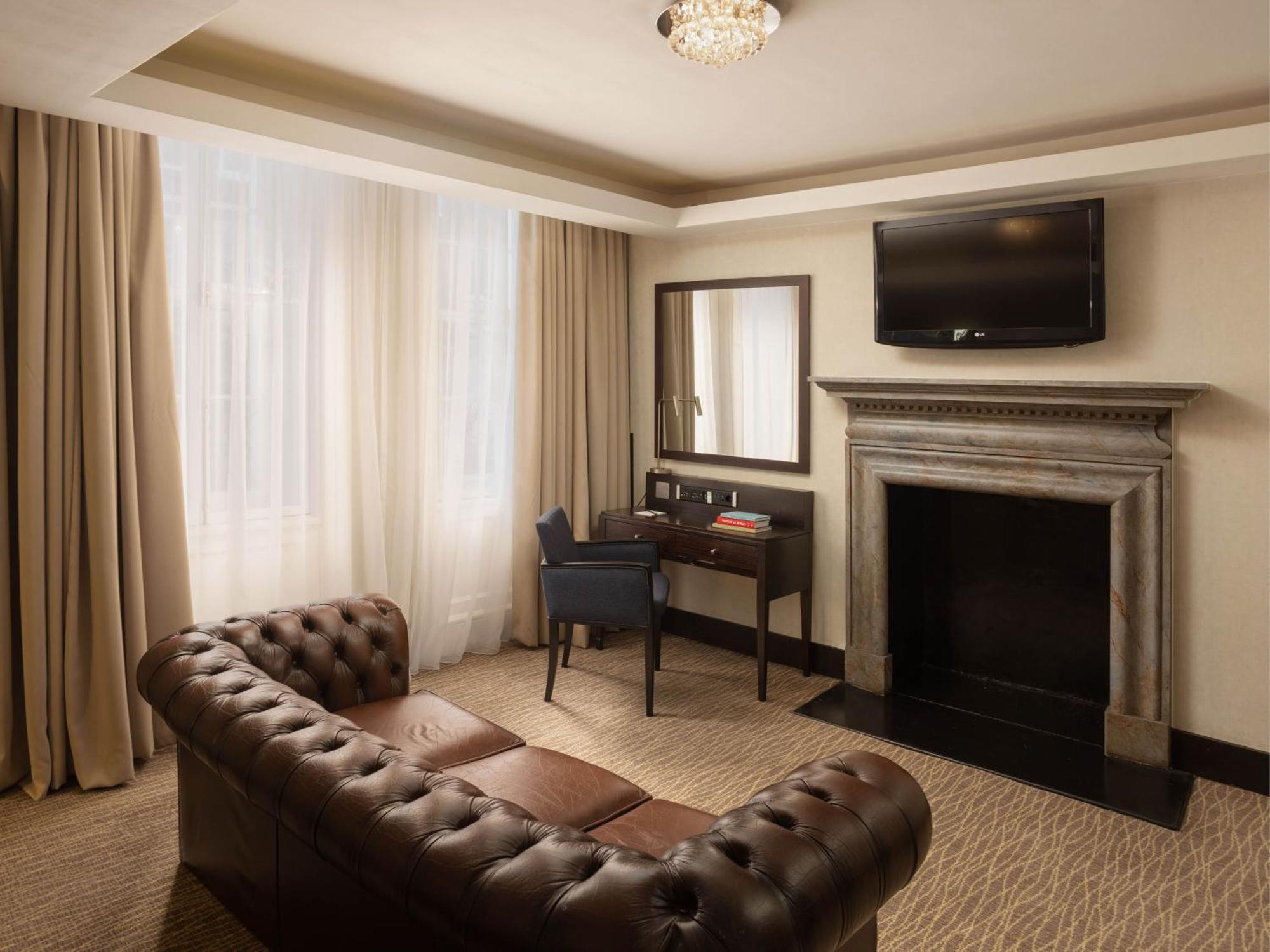Hotel Montcalm Brewery Townhouse Londyn Zewnętrze zdjęcie The photo shows a cozy and elegantly designed room. There is a comfortable brown leather sofa with tufted detailing. A small desk and chair are positioned near a mirror, providing a space for work or personal grooming. On the wall, a flat-screen TV i