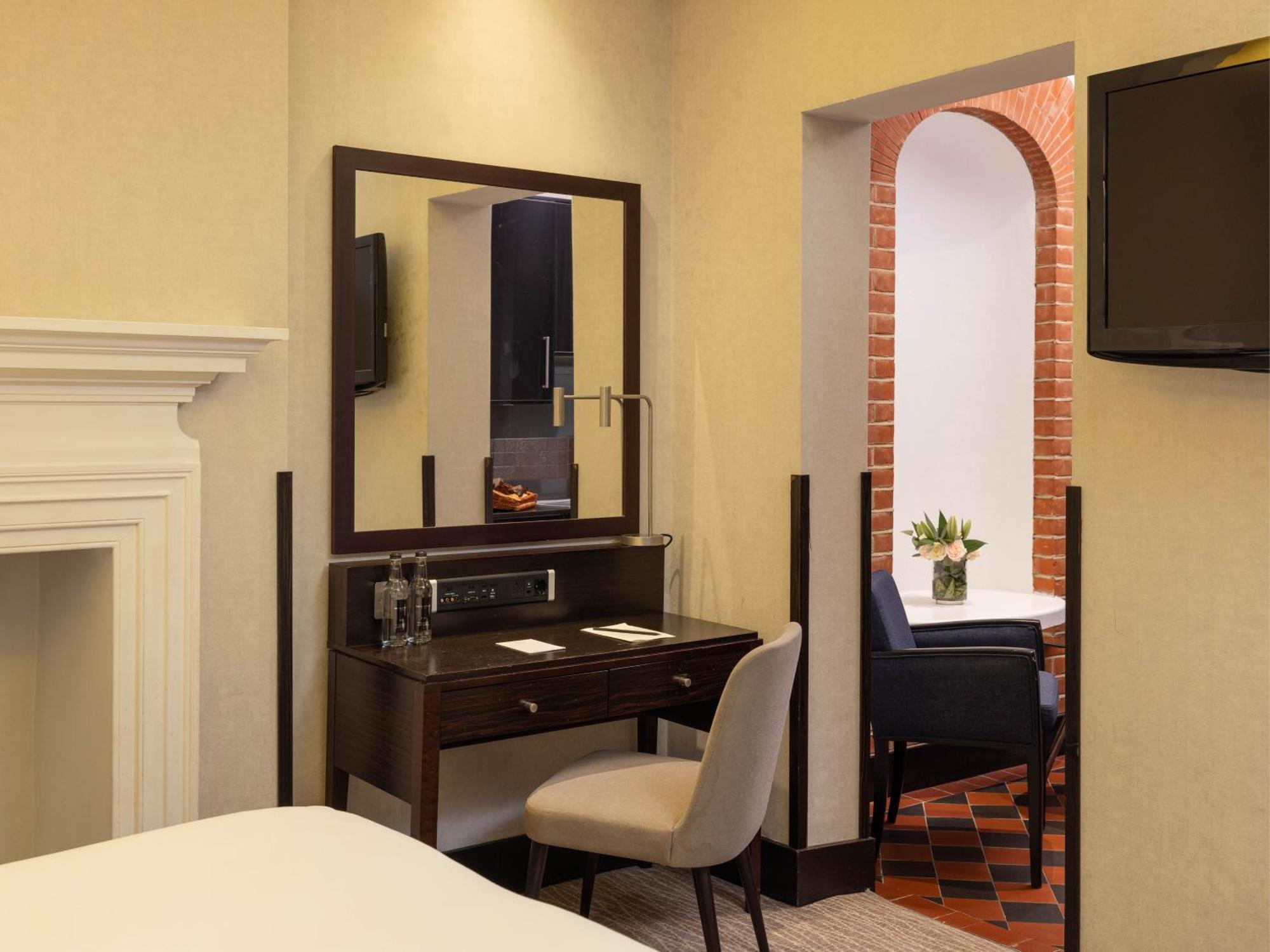 Hotel Montcalm Brewery Townhouse Londyn Zewnętrze zdjęcie The photo displays a hotel room setup. On the left side, there's a bed with a simple white bedding arrangement. Adjacent to the bed, there's a wooden desk with a chair, along with a mirror above the desk. The desk area is equipped with some glassware