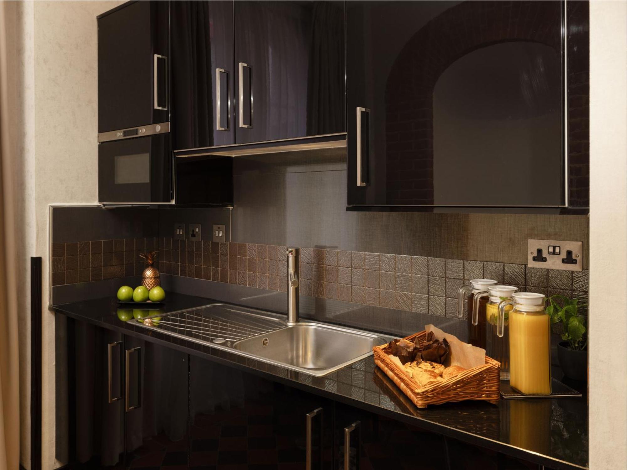 Hotel Montcalm Brewery Townhouse Londyn Zewnętrze zdjęcie The photo shows a modern kitchen with sleek black cabinetry and a glossy finish. The kitchen features a stainless steel sink with a contemporary faucet, set against a dark, textured countertop. Above the counter, there are cabinets that match the cou