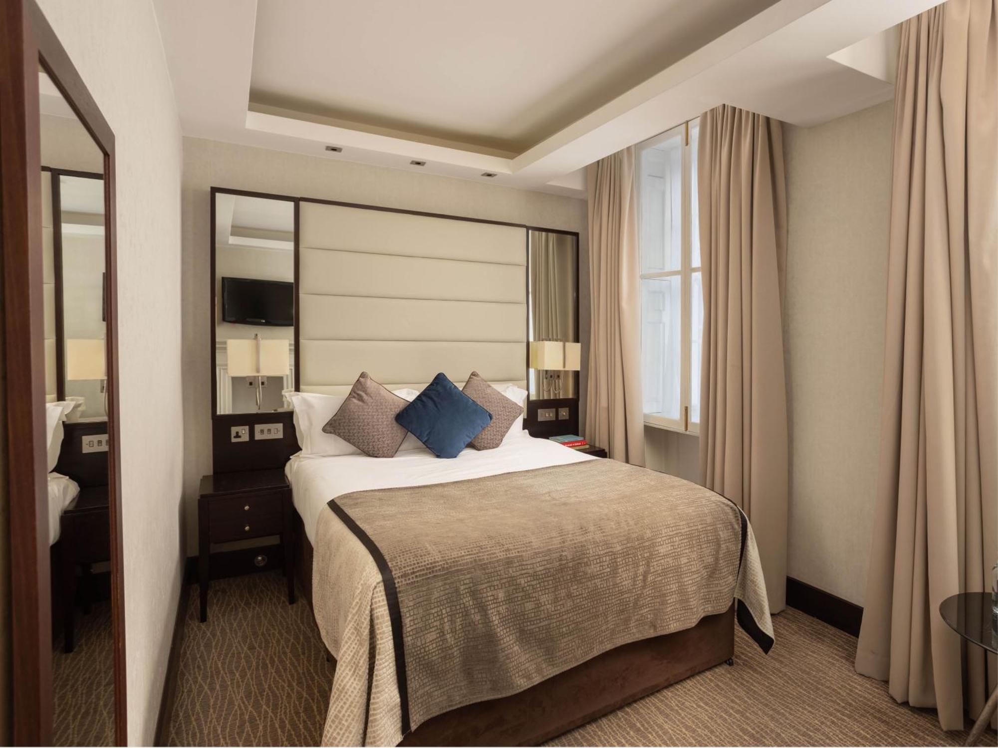 Hotel Montcalm Brewery Townhouse Londyn Zewnętrze zdjęcie The photo shows a cozy hotel room with a bed as the focal point. The bed is made with neutral-colored linens and has several pillows, including a decorative blue one. There are bedside tables on either side of the bed, each with a lamp. A large mirro