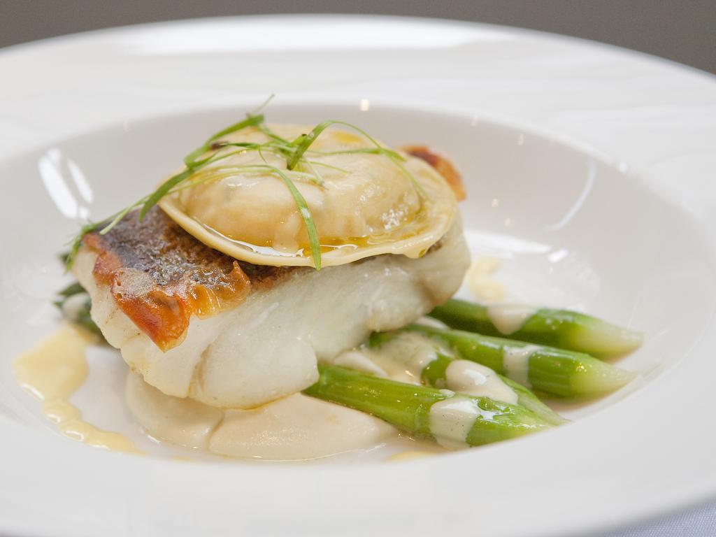 Hotel Montcalm Brewery Townhouse Londyn Zewnętrze zdjęcie The image shows a beautifully presented dish featuring a piece of fish, likely a white fish, topped with a clam. It is served on a bed of green asparagus spears. The dish is garnished with thinly sliced herbs or greens, adding a touch of color. The s