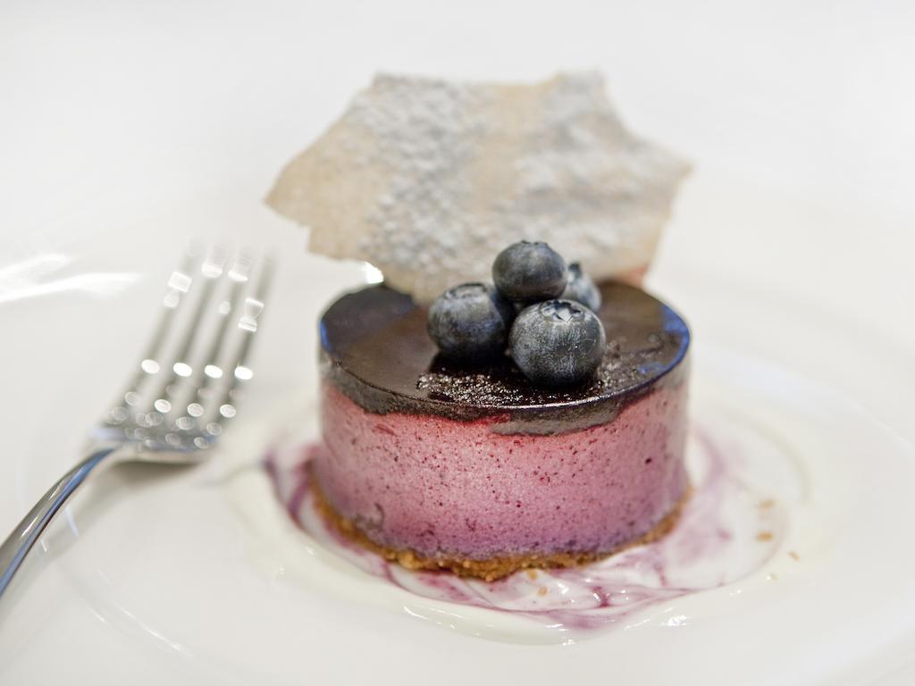Hotel Montcalm Brewery Townhouse Londyn Zewnętrze zdjęcie The photo shows a beautifully plated dessert, which appears to be a round cheesecake or mousse. It has a pinkish-purple filling, topped with a glossy dark chocolate layer. Three fresh blueberries sit on top, adding a pop of color. The dessert is acco