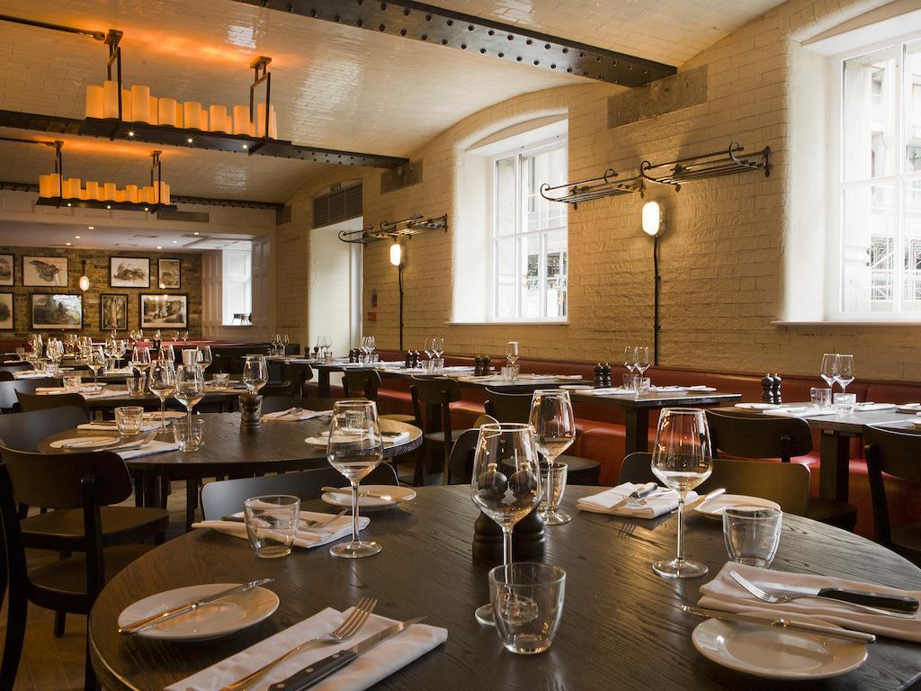 Hotel Montcalm Brewery Townhouse Londyn Zewnętrze zdjęcie The photo shows a restaurant interior featuring a warm and inviting atmosphere. It has several round wooden tables set for dining, each with neatly arranged plates, utensils, and glasses. The lighting is soft, with overhead fixtures providing a cozy 