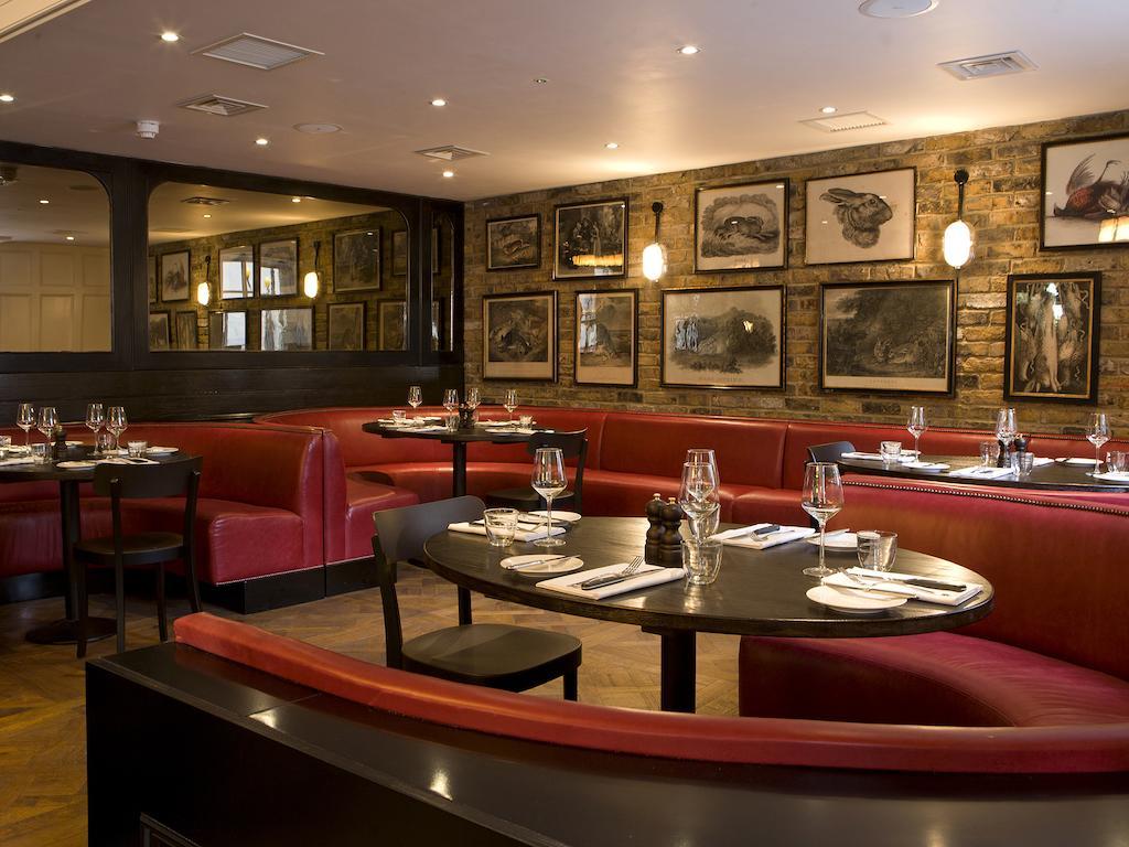 Hotel Montcalm Brewery Townhouse Londyn Zewnętrze zdjęcie The photo depicts an elegant restaurant interior. There are curved red booths along the walls, creating a cozy seating arrangement. The tables are round and set with white plates and glassware, indicating a prepared dining area. The walls feature a n
