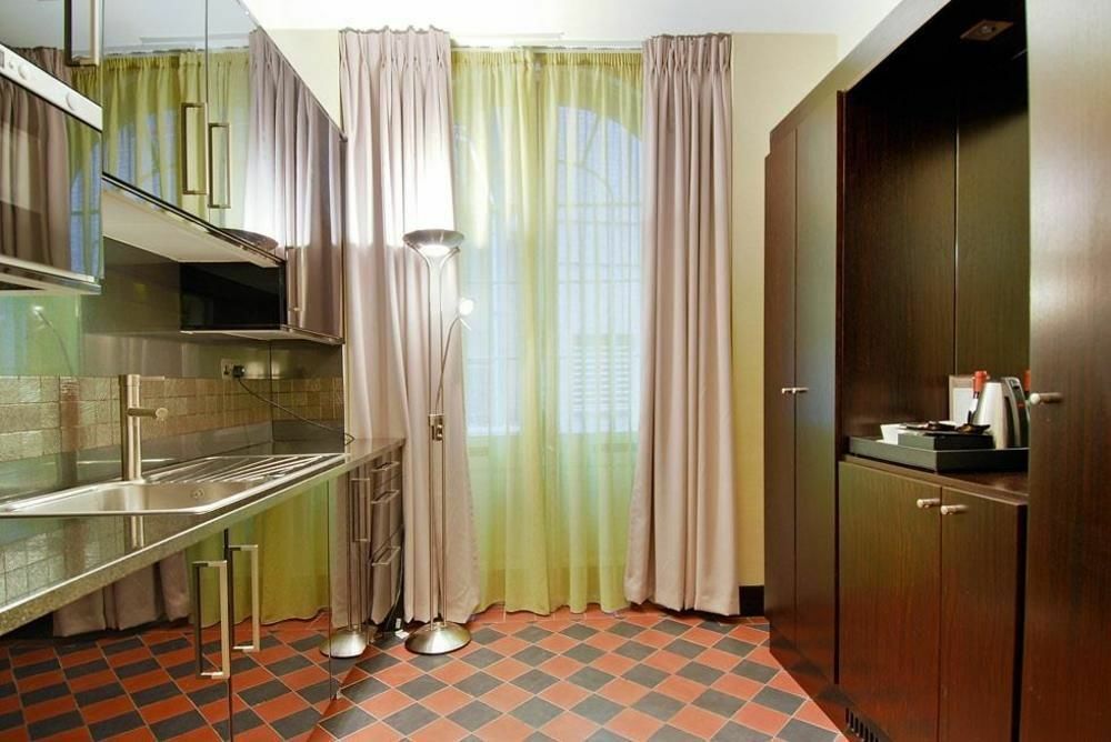 Hotel Montcalm Brewery Townhouse Londyn Zewnętrze zdjęcie The photo shows a modern kitchen area. There is metallic cabinetry and a stainless steel countertop with a sink. The walls are adorned with light-colored curtains that allow natural light to filter in, with one set in a soft purple hue and another in